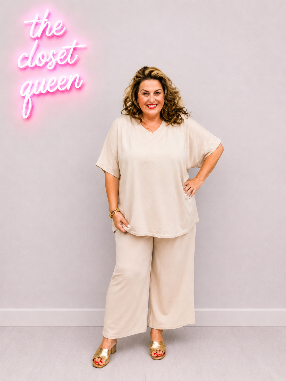 Woman in a beige outfit standing in front of a neon sign with 'the closet queen' text.