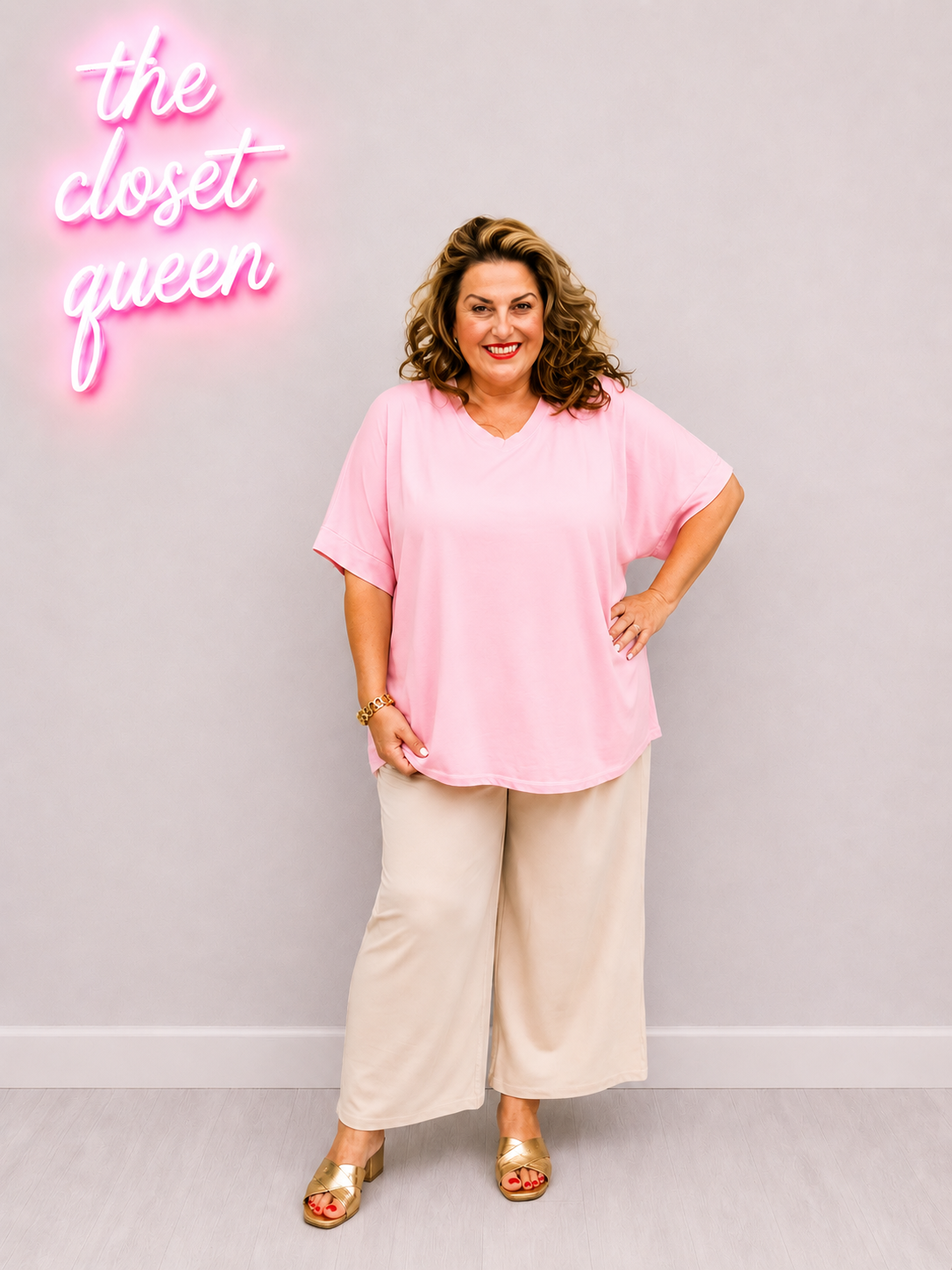 Woman wearing a pink top and beige pants with a neon sign in the background.