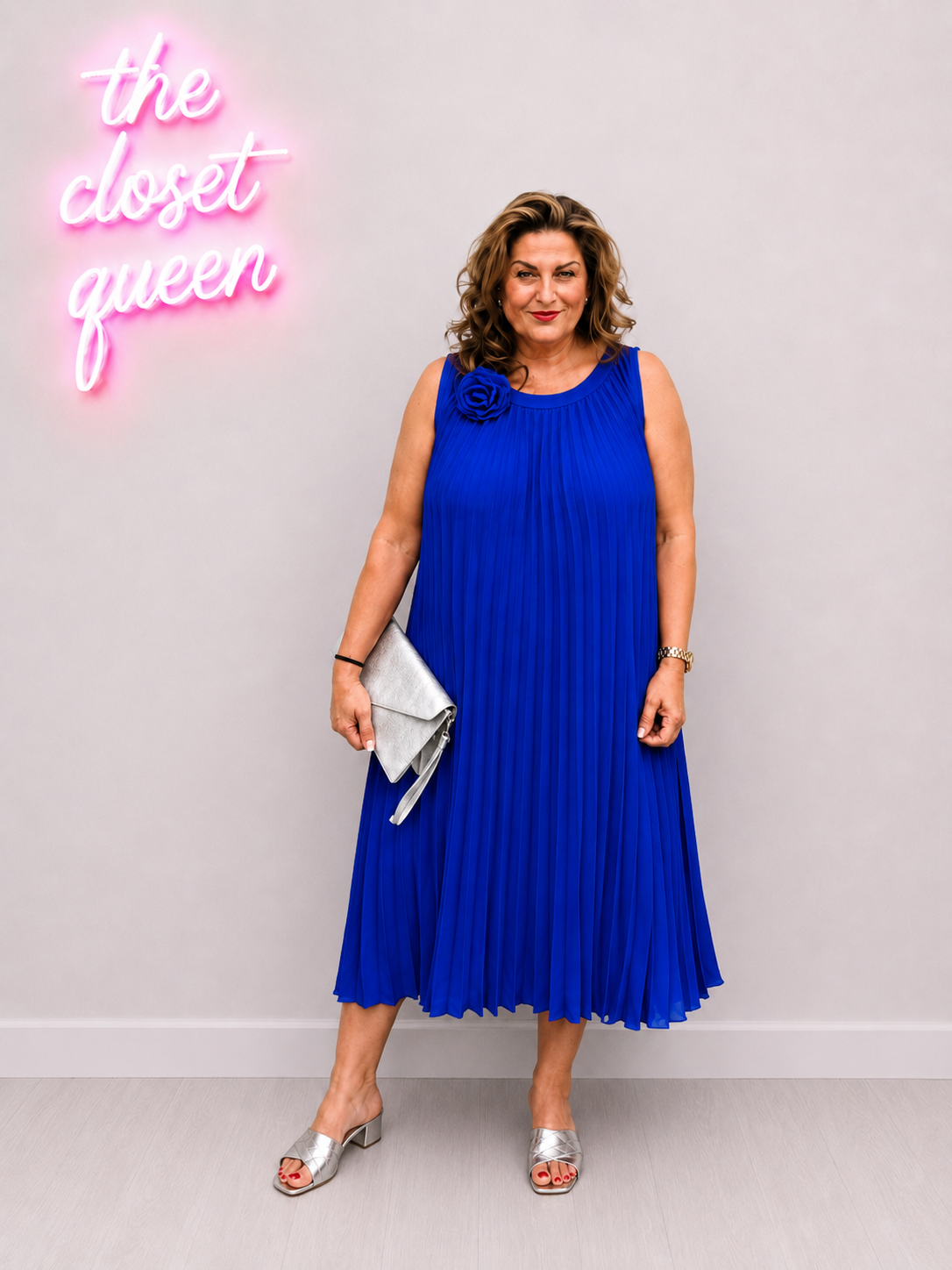 Woman in a blue dress standing in front of a neon sign with 'the closet queen' text.