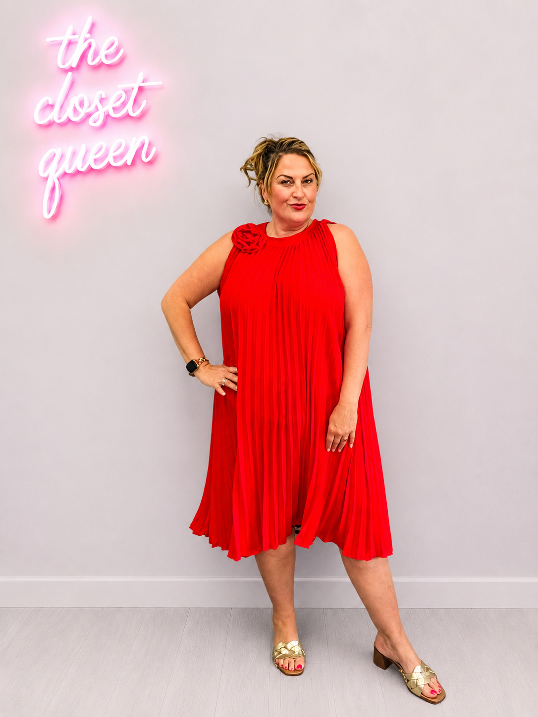 Woman in a red dress standing in front of a gray wall with a neon sign that reads 'the closet queen'.