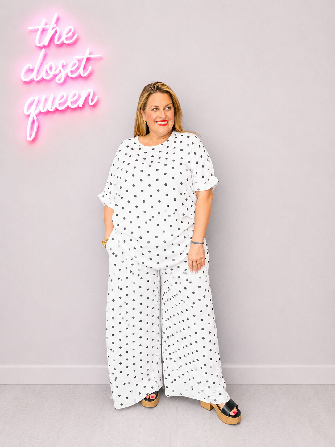 Woman wearing a white polka dot outfit with a neon sign in the background.